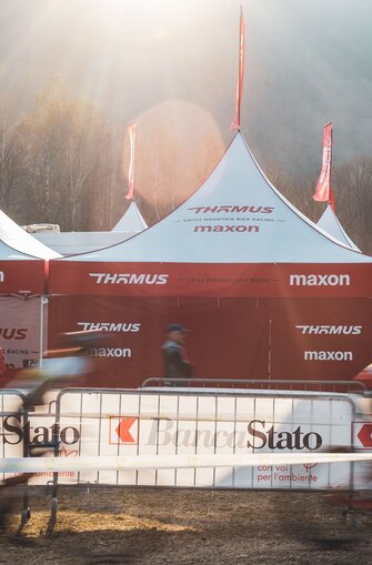 A line of 17x17ft Mastertent canopy tents set up alongside a cycling race and printed in the Thomus-Maxon team branding.