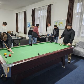 2 Jungen spielen im Vordergrund Billiard, im Hintergrund spielen 2 weitere Tischtennis und 4 weitere Tischkicker.