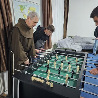 3 Jungen spielen gemeinsam mit einem Franziskanermönch Tischkicker.